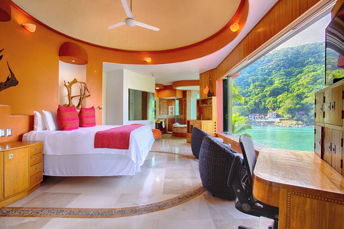 Una habitación de hotel moderna con una cama grande, un escritorio y vistas a un paisaje tropical.