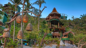 Un resort tropical con construcciones de techo de paja, cestas colgantes de mimbre y exuberante follaje.