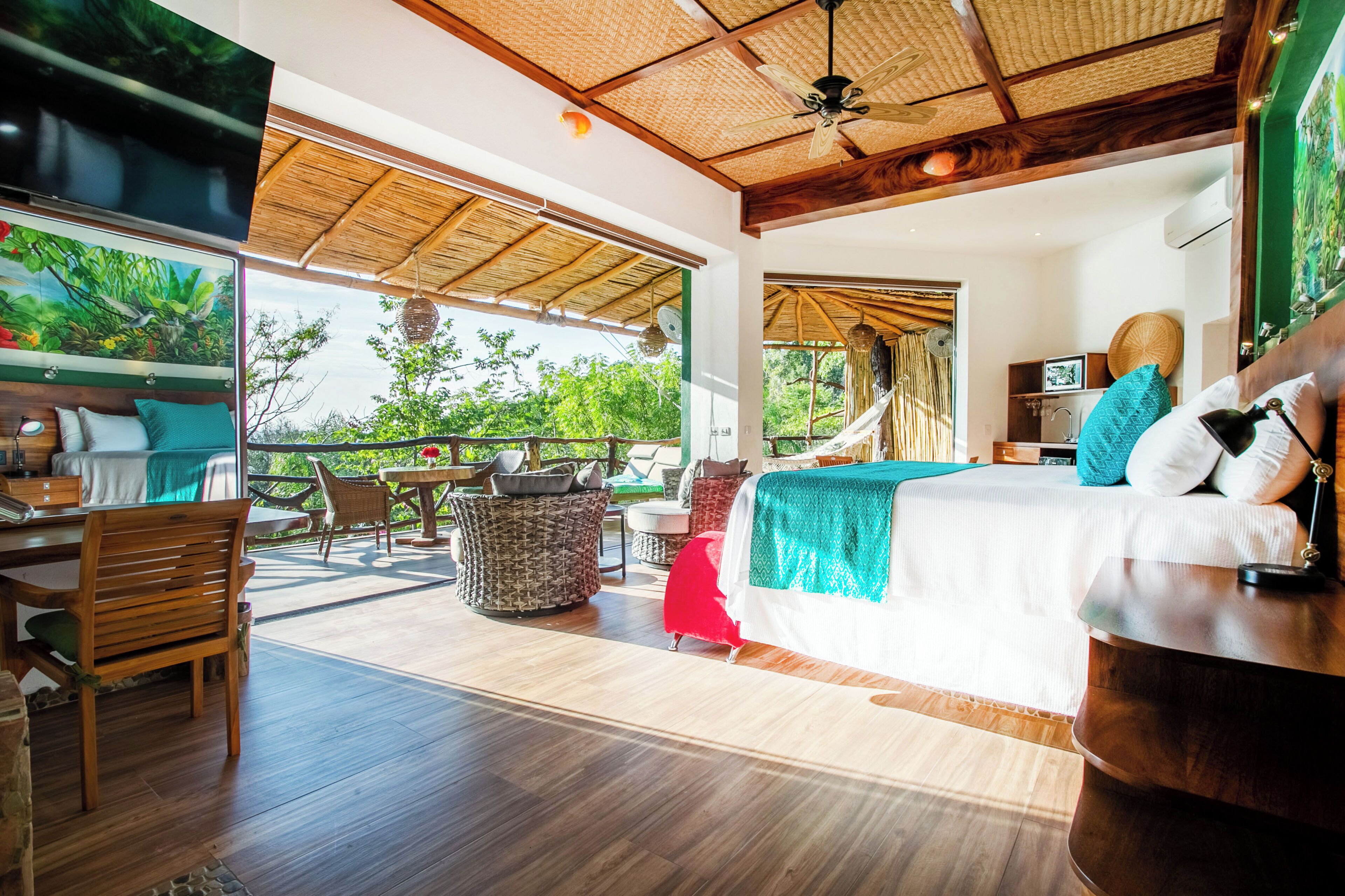 A spacious room with a bed, a desk, and a chair, a ceiling fan, and a view of greenery outside.