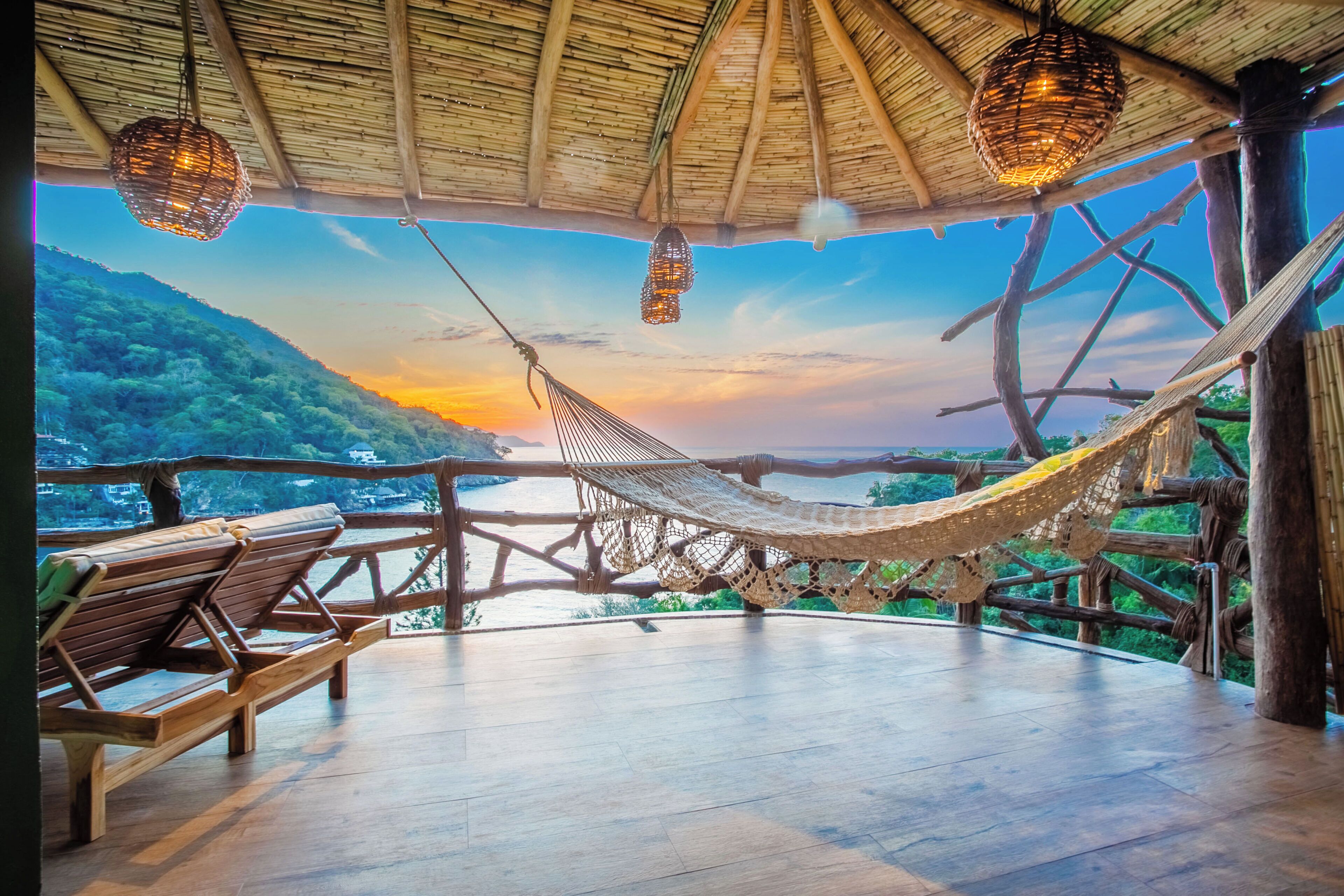 A hammock under a thatched roof, wooden benches, and a view of a river and hills.