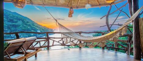 A hammock under a thatched roof, wooden benches, and a view of a river and hills.