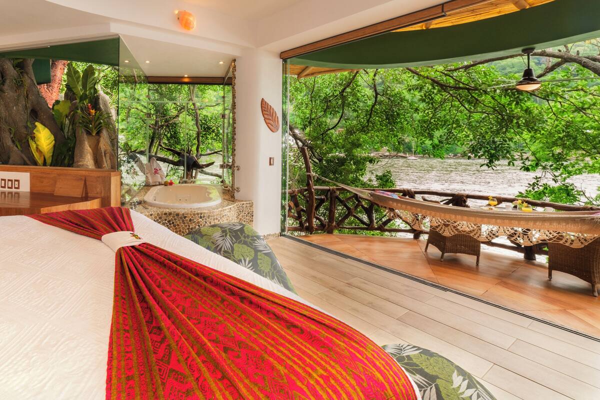 Un dormitorio con una cama grande, un baño con bañera y vistas a un jardín exuberante.
