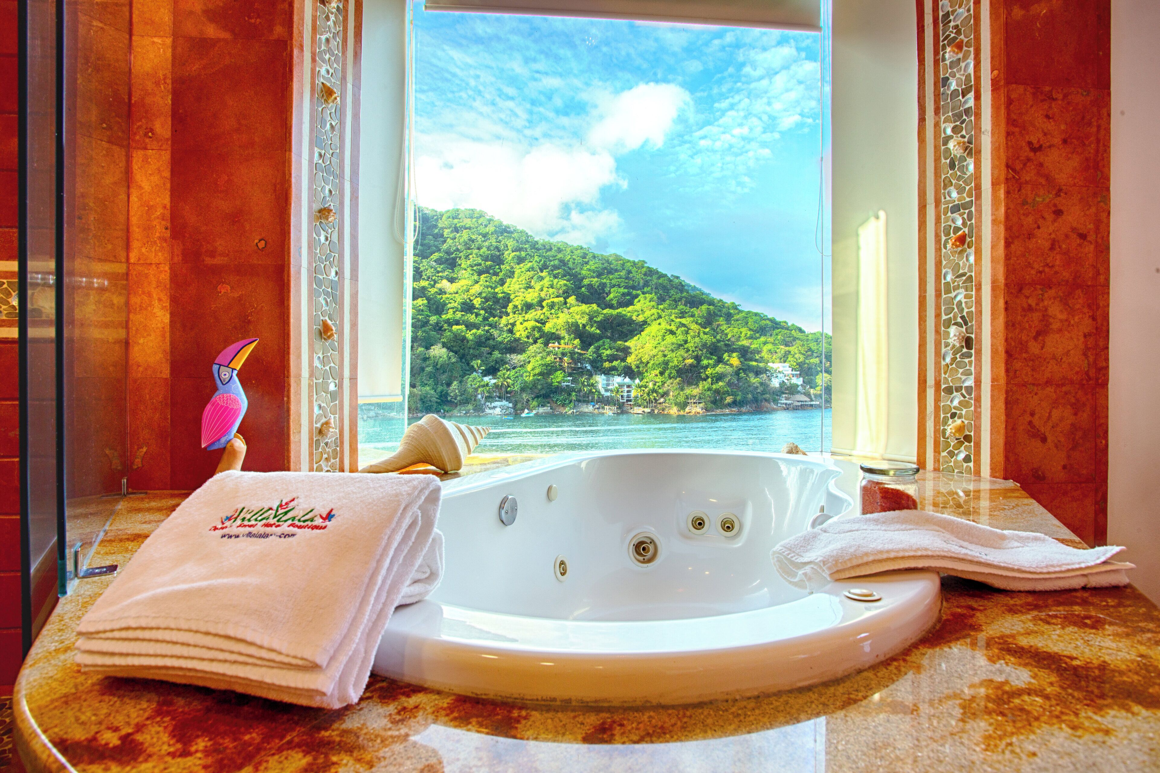 Un baño con bañera, toallas y vistas a una isla boscosa a través de una ventana.