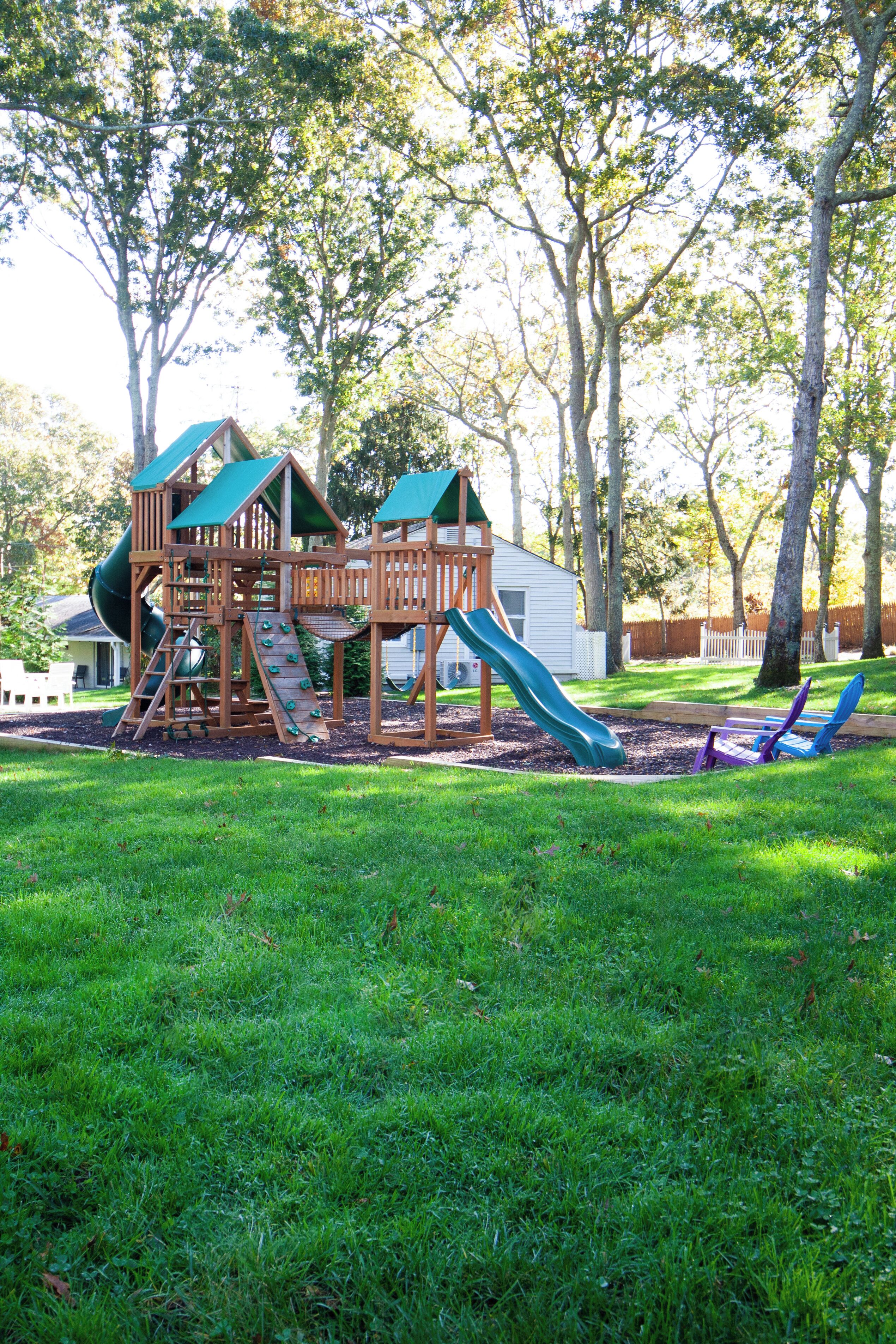 Un parque infantil de madera con toboganes y estructuras para escalar, rodeado de césped y árboles.