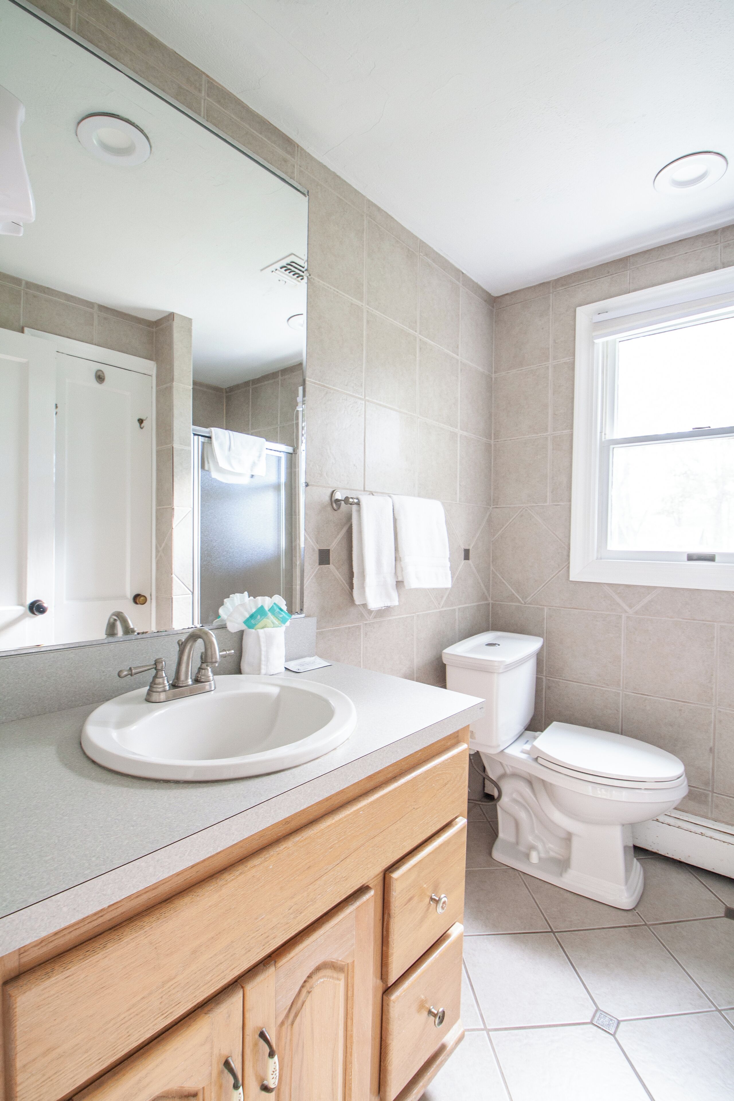 Een moderne badkamer met een wastafel, spiegel, toilet en raam.