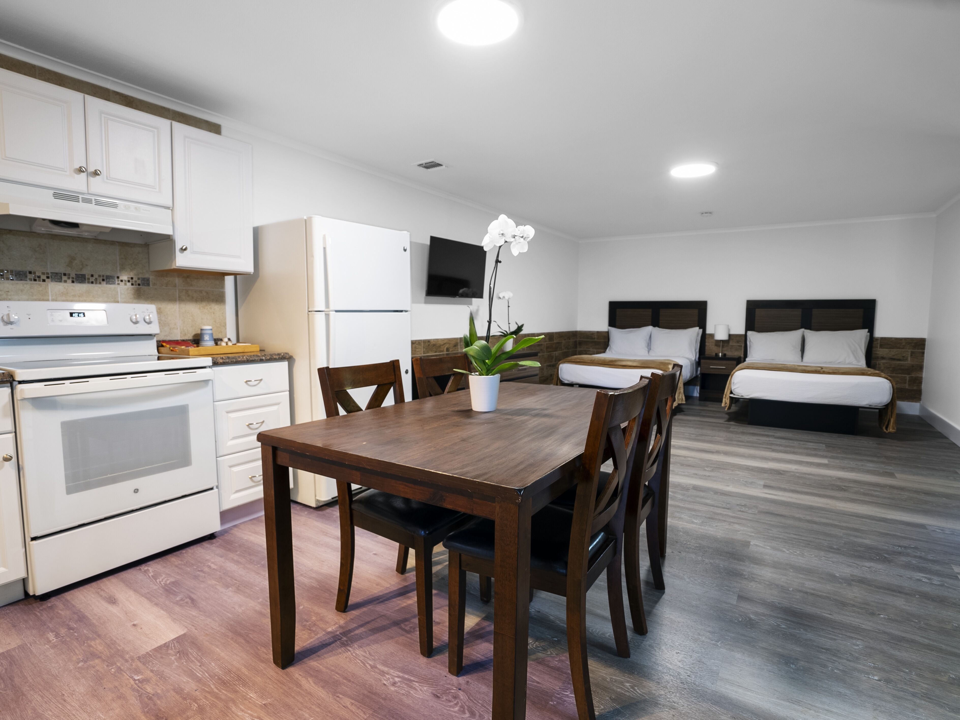 A modern kitchen with white appliances, a dining table with chairs, and a small potted plant.