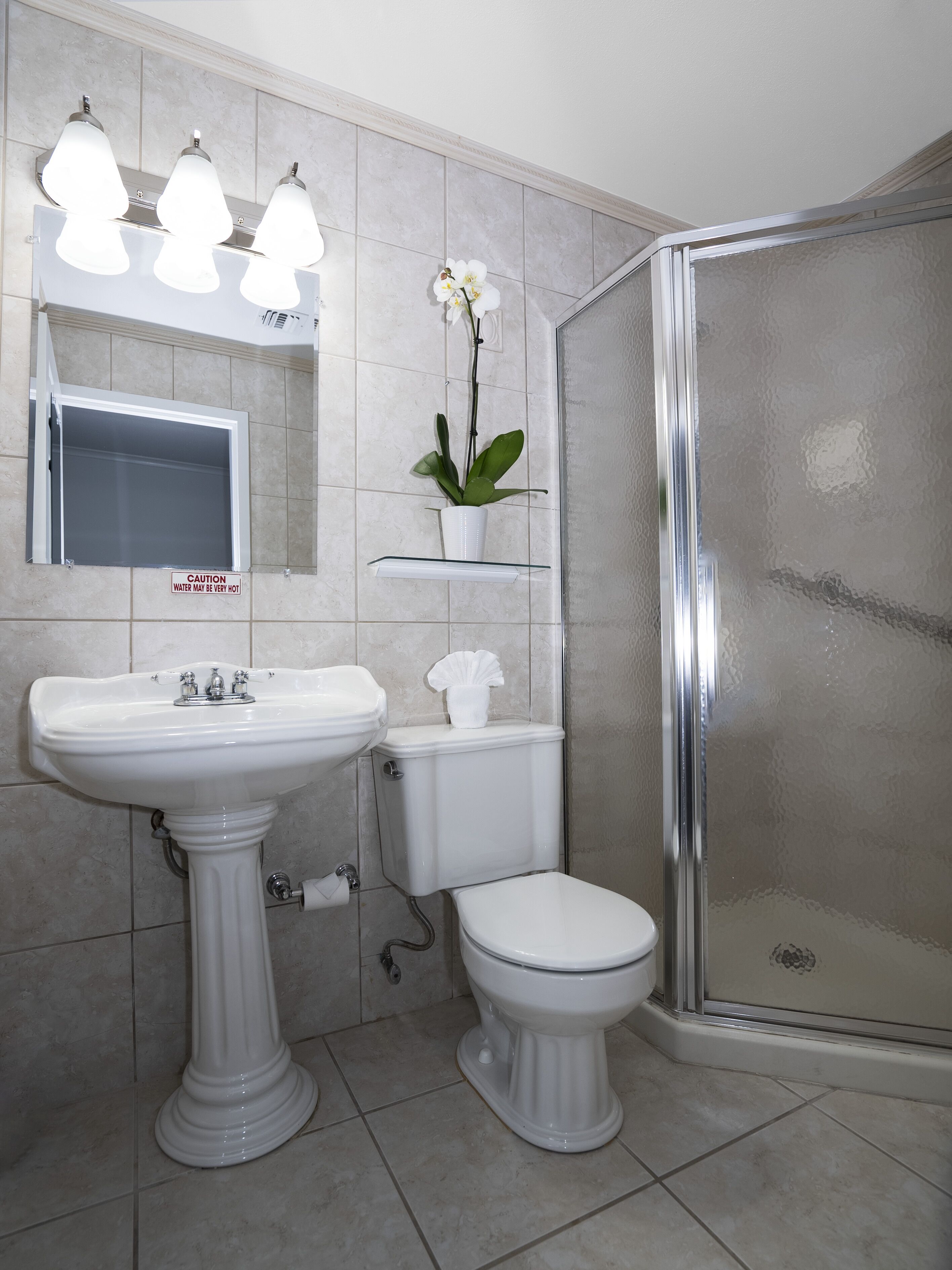 A bathroom with a pedestal sink, toilet, and a glass shower enclosure.