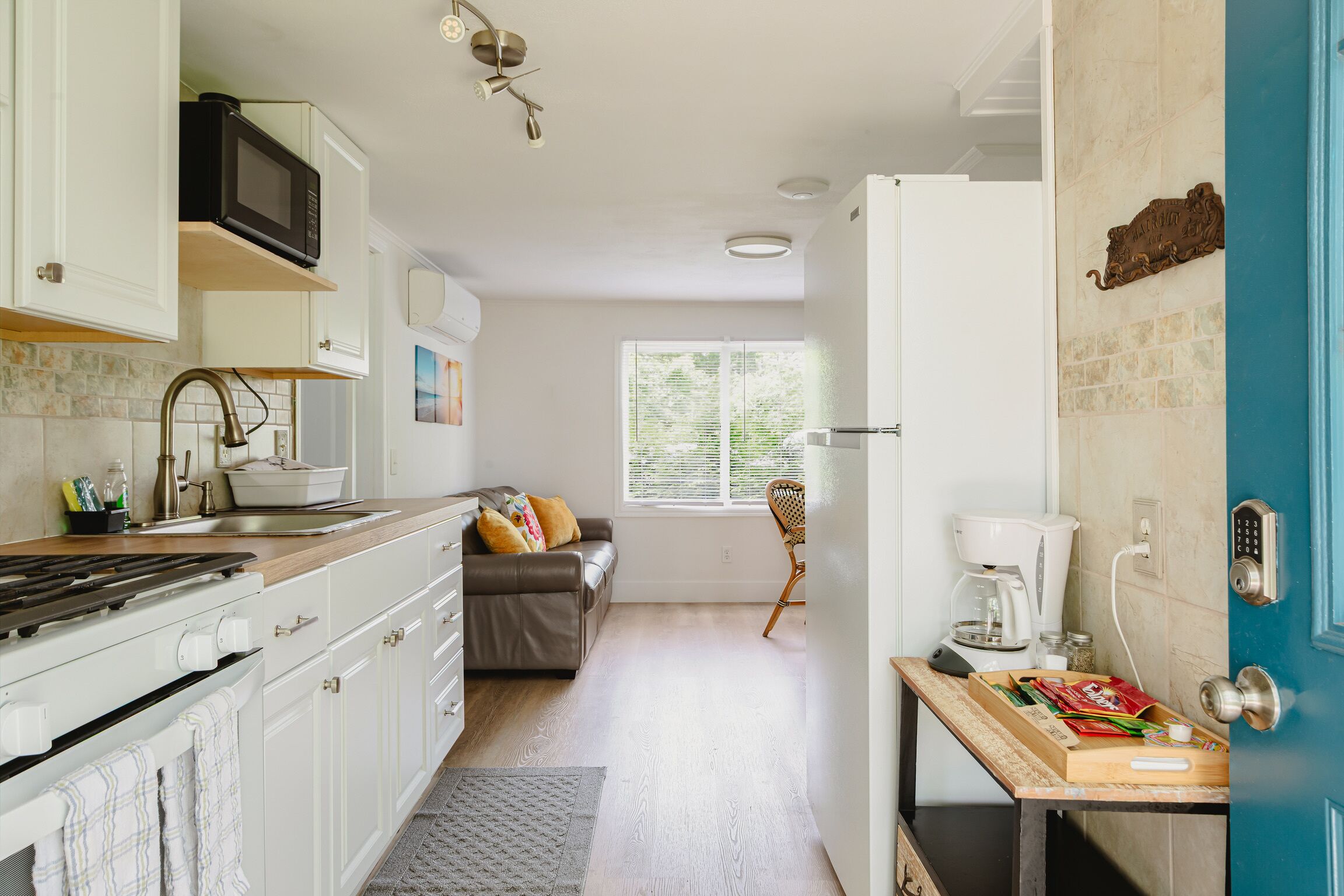 A kitchen with a stove, microwave, and sink; a dining area with a table and chairs; a sofa; and a window with blinds.