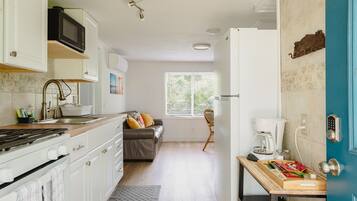 A kitchen with a stove, microwave, and sink; a dining area with a table and chairs; a sofa; and a window with blinds.