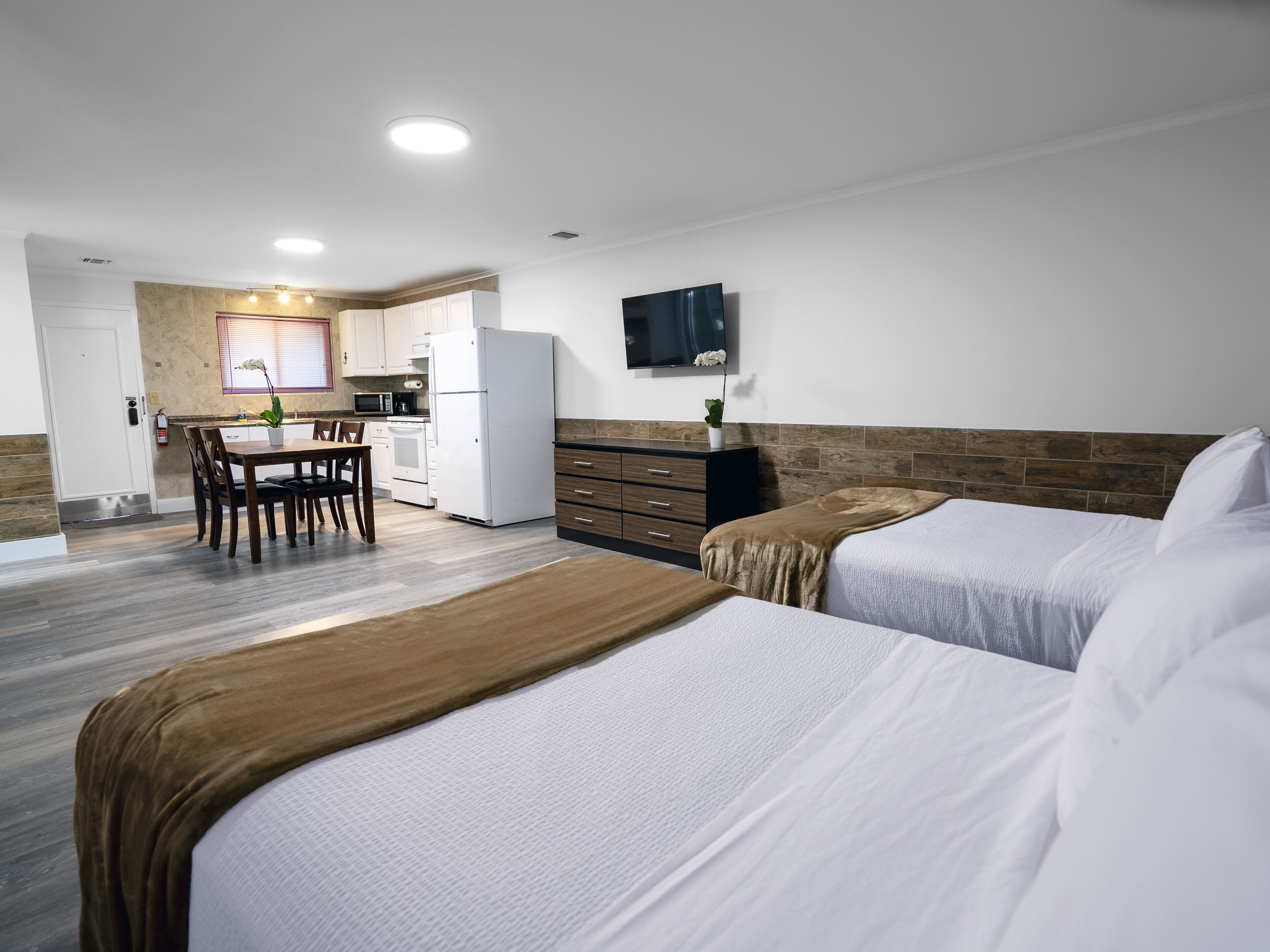 Une chambre d’hôtel avec deux lits, une petite kitchenette, une table à manger et un téléviseur fixé au mur.