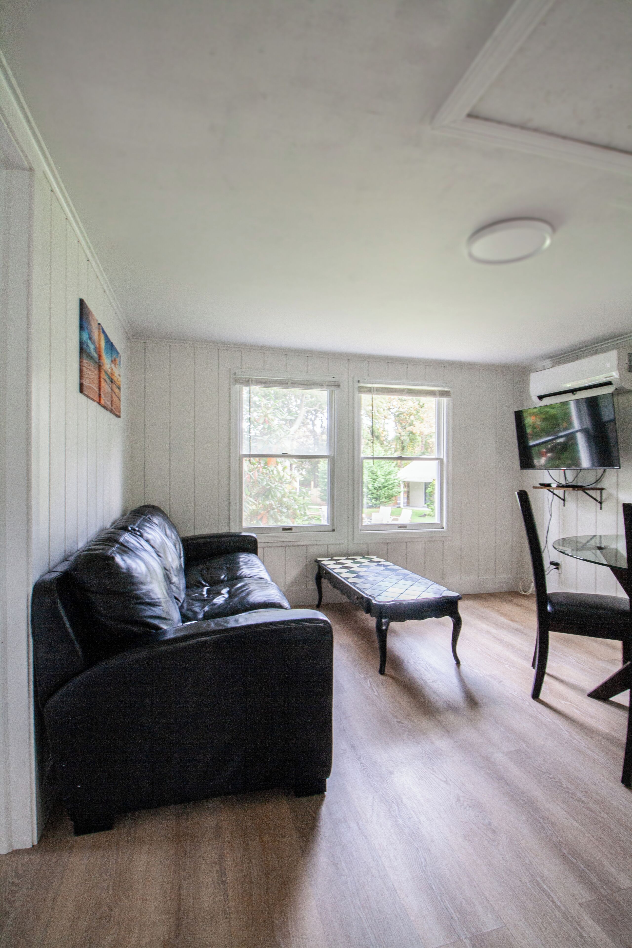 Une pièce avec un canapé en cuir noir, une petite table et un téléviseur fixé au mur.