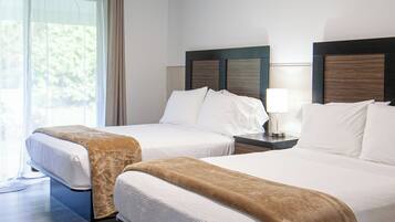 A hotel room with two beds, a large window with curtains, a ceiling light, and a wooden floor.