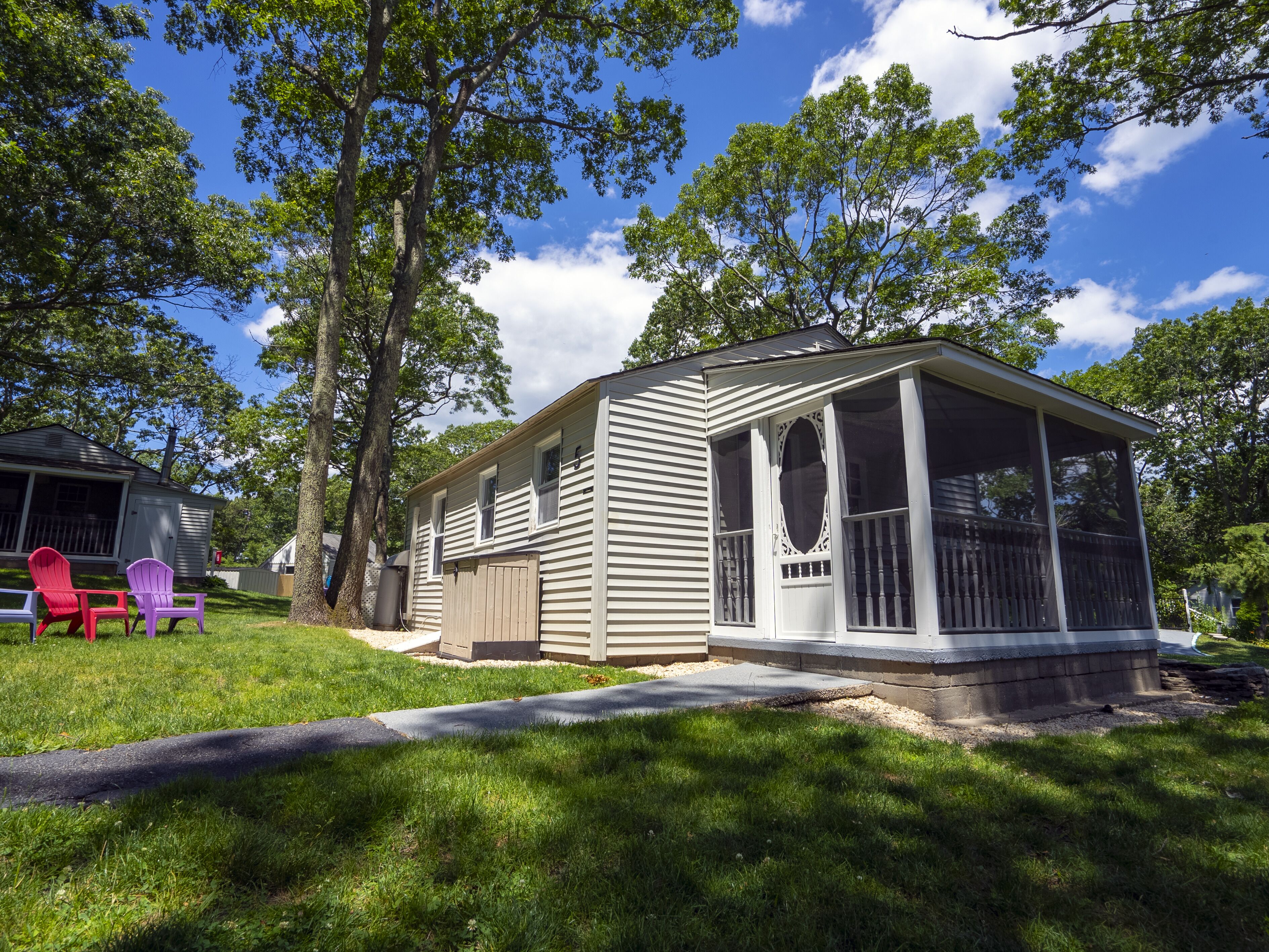 A single-story mobile home with a porch and screened windows, surrounded by trees and a grassy yard.