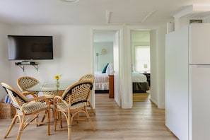 A dining area with wicker chairs, a glass table, and a flat-screen TV mounted on the wall. - Hampton's Vacation Inn (Hampton Bays)