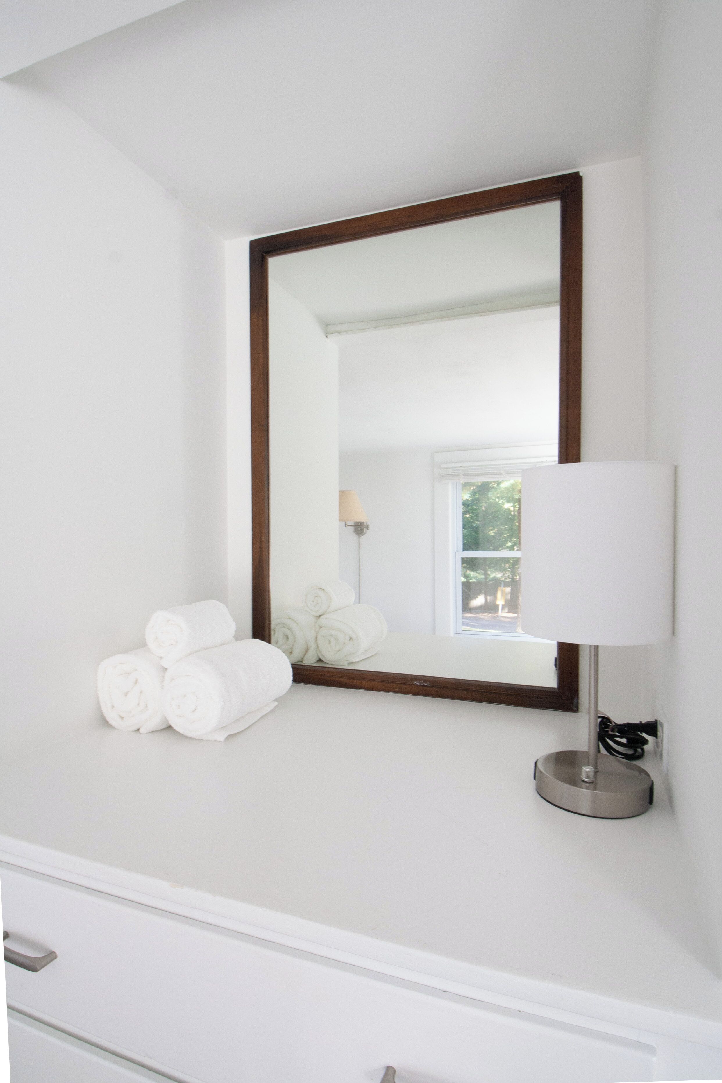 A bathroom with a large mirror, a white countertop, and rolled towels.