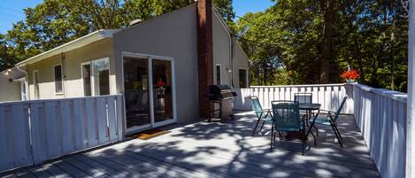 Une terrasse couverte avec une clôture blanche, une cheminée en briques et une table entourée de chaises.