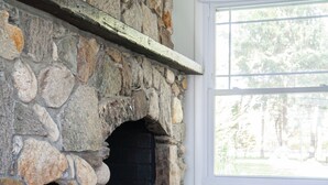Una chimenea de piedra con un banco incorporado, un ventanal con vistas a árboles y un suelo de piedra.