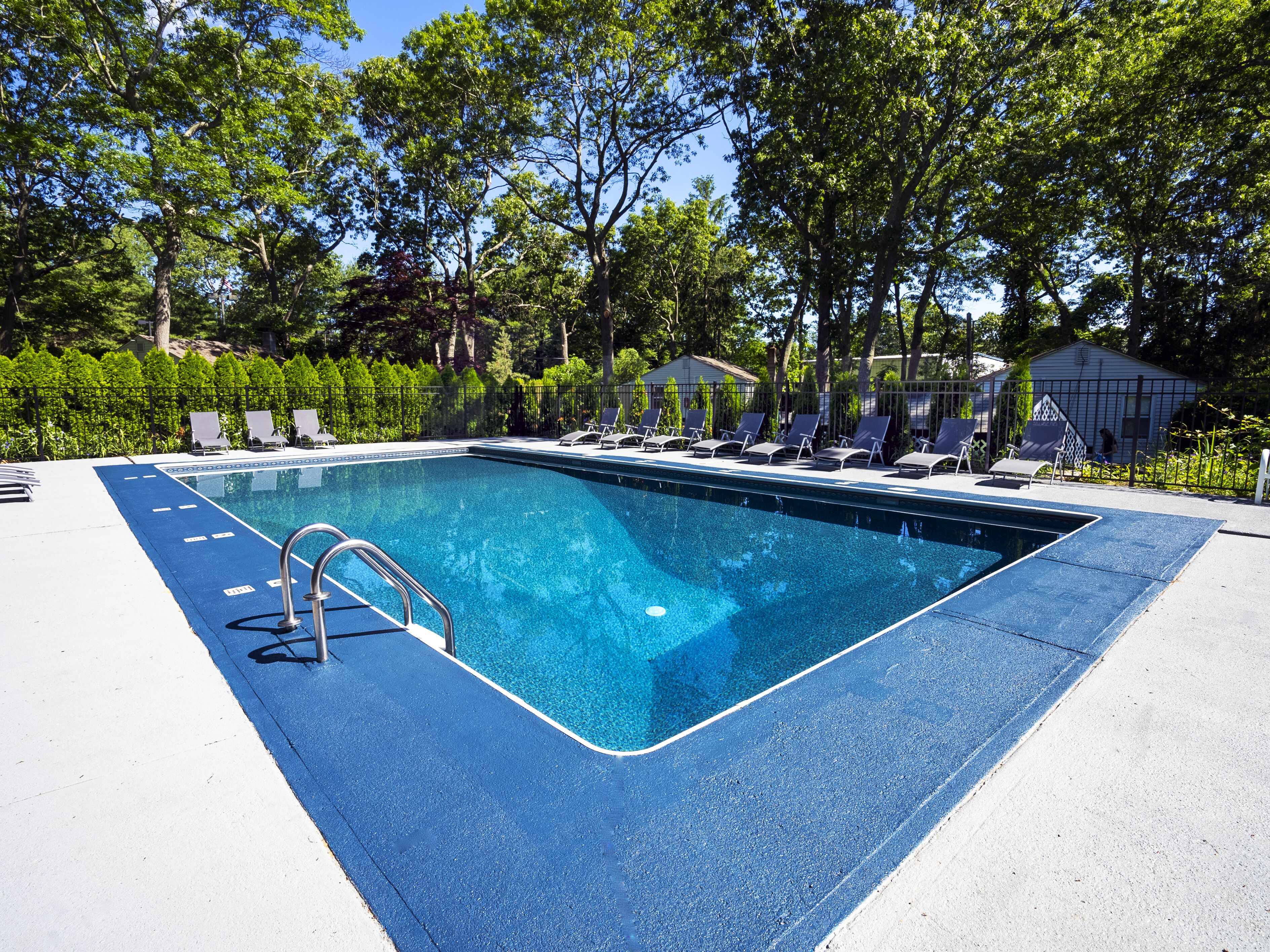 Une piscine rectangulaire avec un bord bleu, entourée de chaises longues et d’une échelle en métal.
