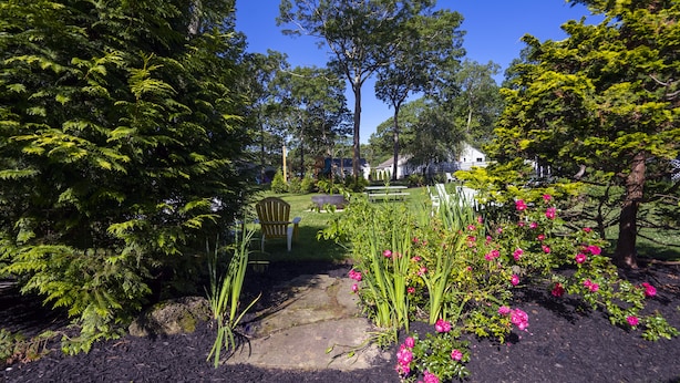 Un jardín con un banco de madera, un parque infantil y una casa al fondo.