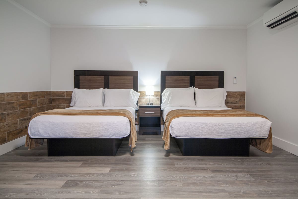 A hotel room with two beds, a nightstand, and a lamp.