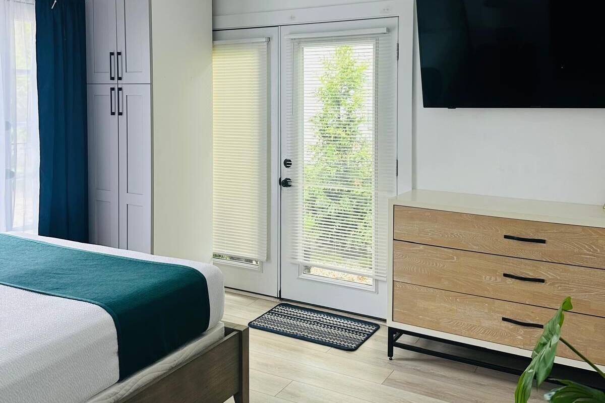 A modern bedroom with a bed, wardrobe, TV, and a view through a door.