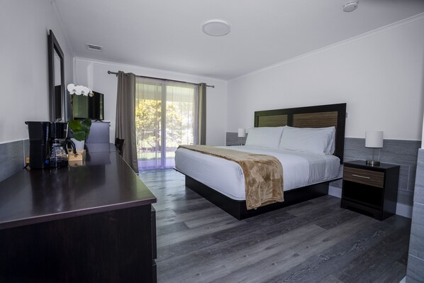 A modern hotel room with a large bed, a desk with a coffee machine, a TV, and a view of the outdoors. - Hampton's Vacation Inn (Hampton Bays)