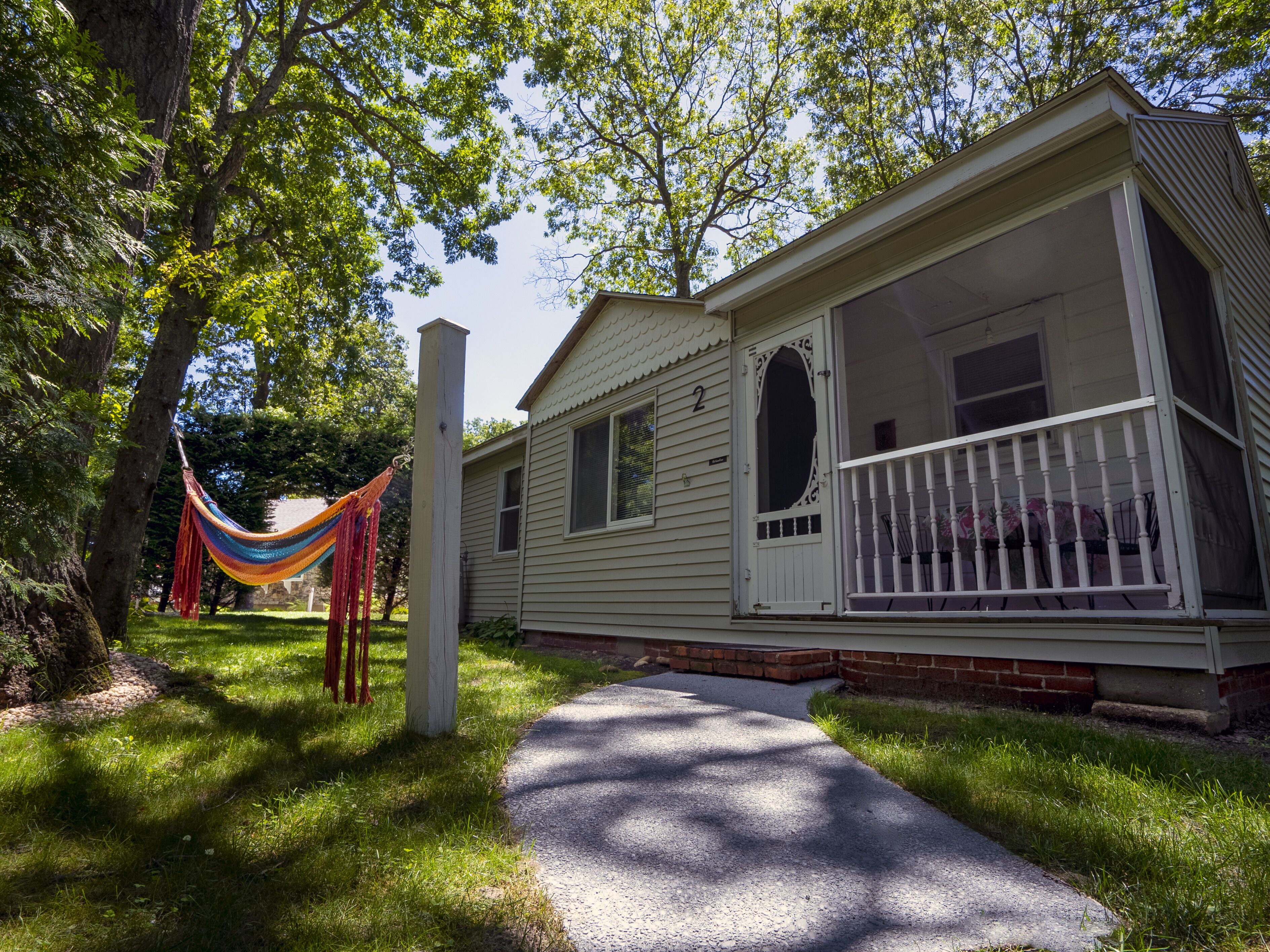 A single-story house with a porch, a visible number '2' on the door, and a hammock hanging between two trees.