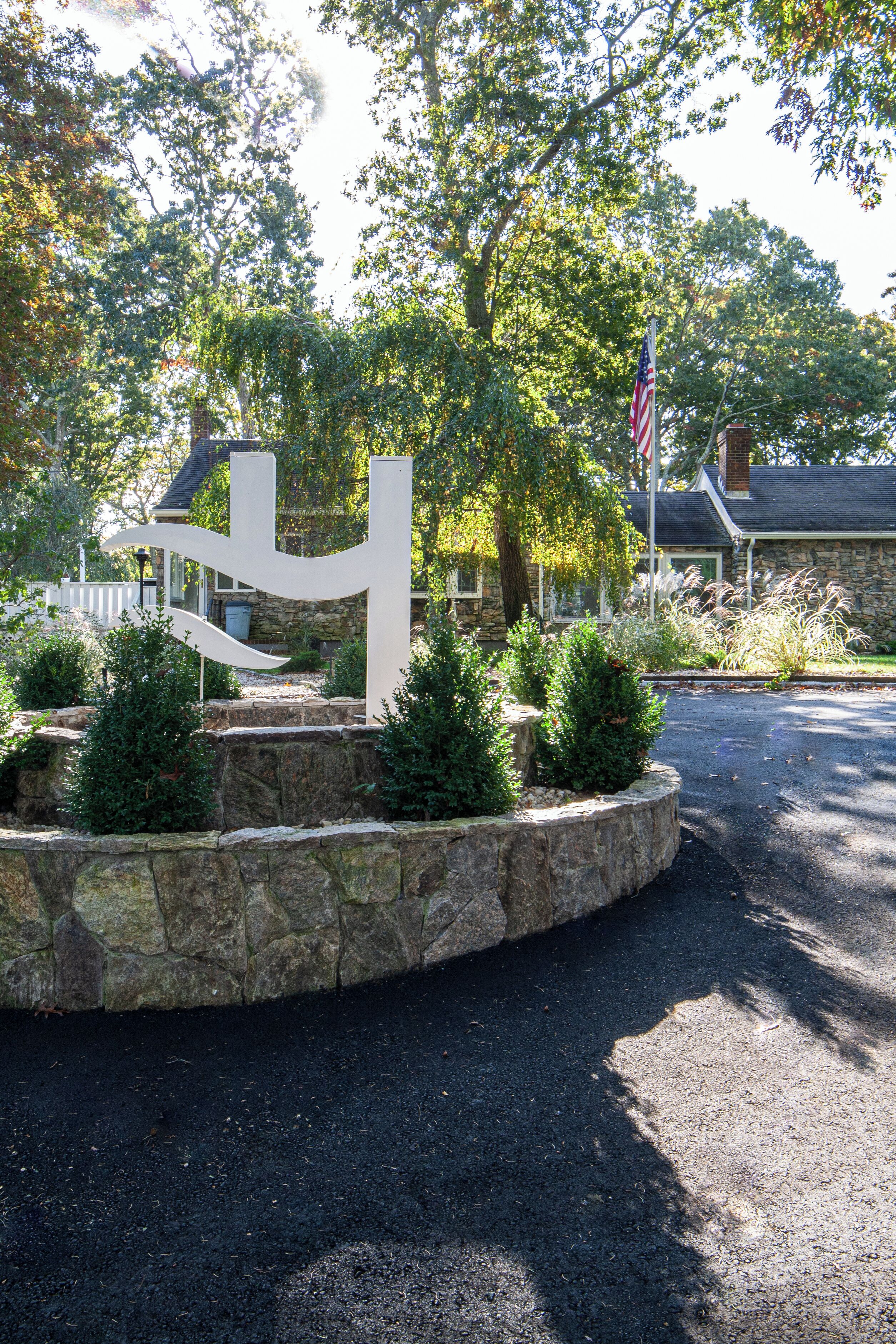A stone wall with a flag, surrounded by greenery and a building in the background.