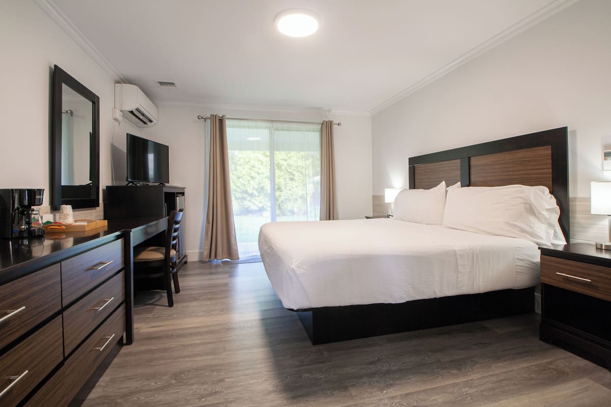A modern hotel room with a large bed, a desk with a chair, a flat-screen TV, and a window with curtains.