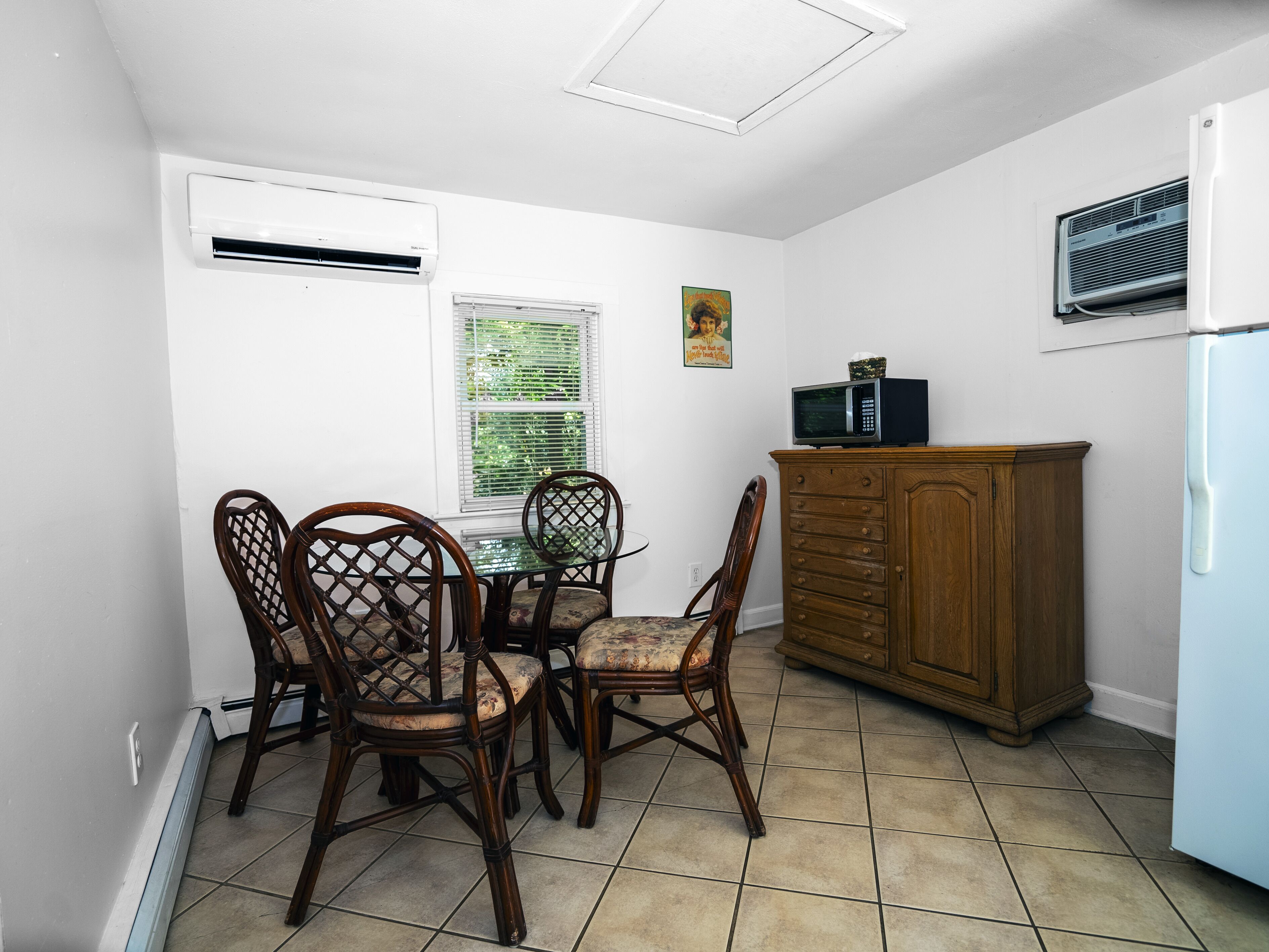 A compact kitchen with a dining table, chairs, a wooden cabinet, and an air conditioner.