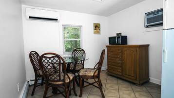 A compact kitchen with a dining table, chairs, a wooden cabinet, and an air conditioner.