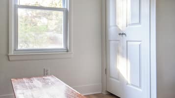Una habitación con una mesa de madera, una puerta blanca y una ventana con persianas.