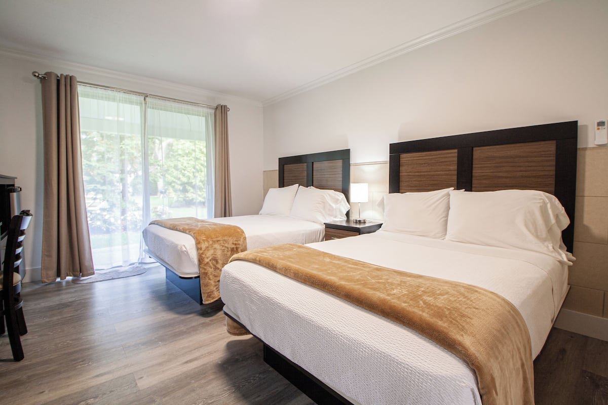 A hotel room with two beds, a desk, and a large window with curtains.
