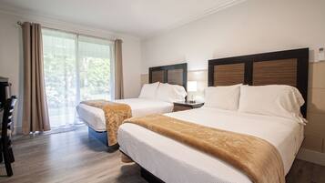 A hotel room with two beds, a desk, and a large window with curtains.