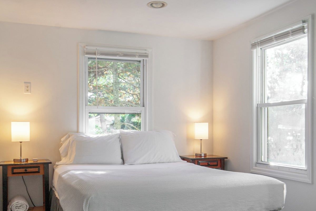 A bedroom with a bed, two bedside tables, a window, and a nightstand.