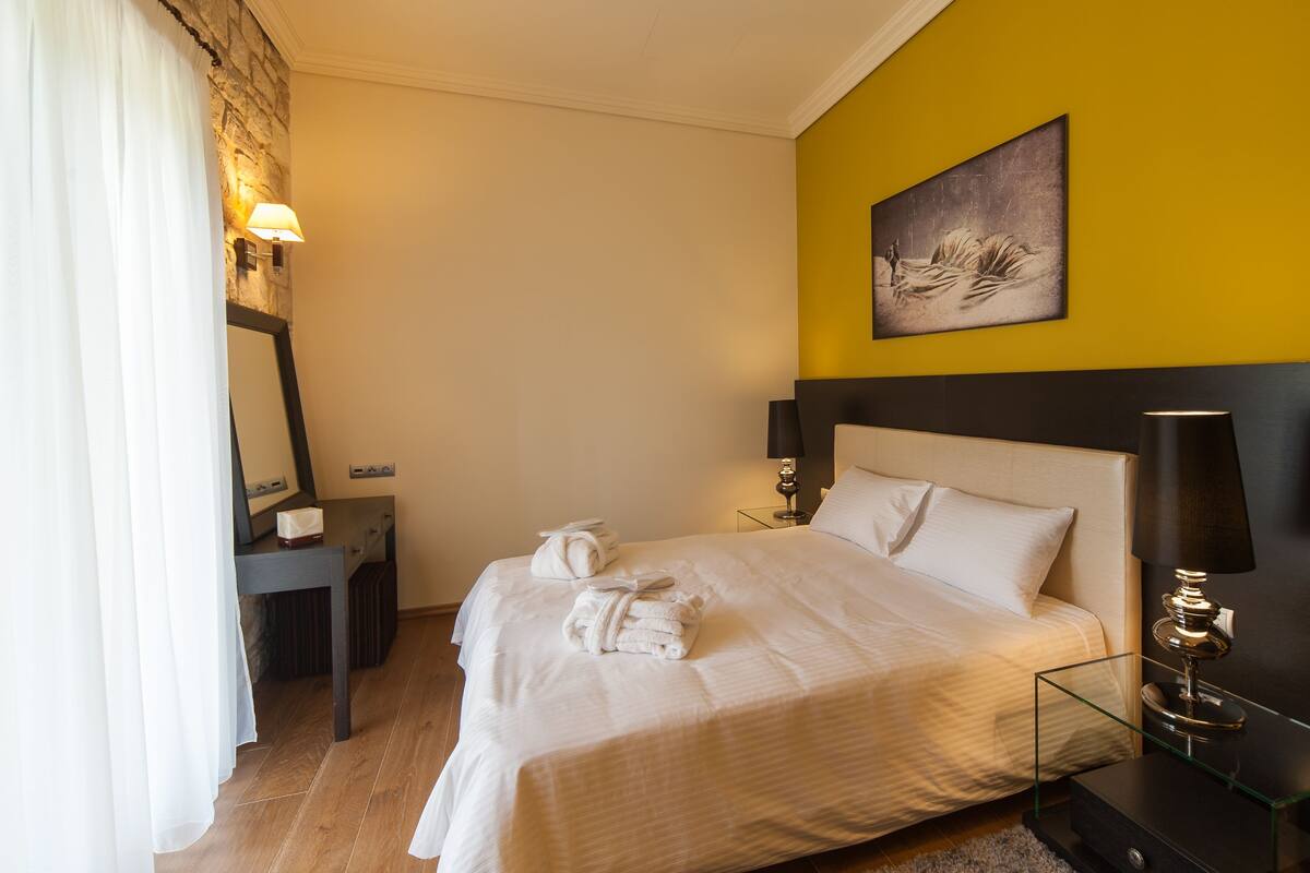 A hotel room with a bed, bedside lamps, a desk with a lamp, a painting on the wall, and a curtain.