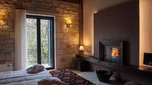 Ein gemütliches Zimmer mit Steinwand, Kamin, einem Bett mit Decke und Blick ins Grüne.