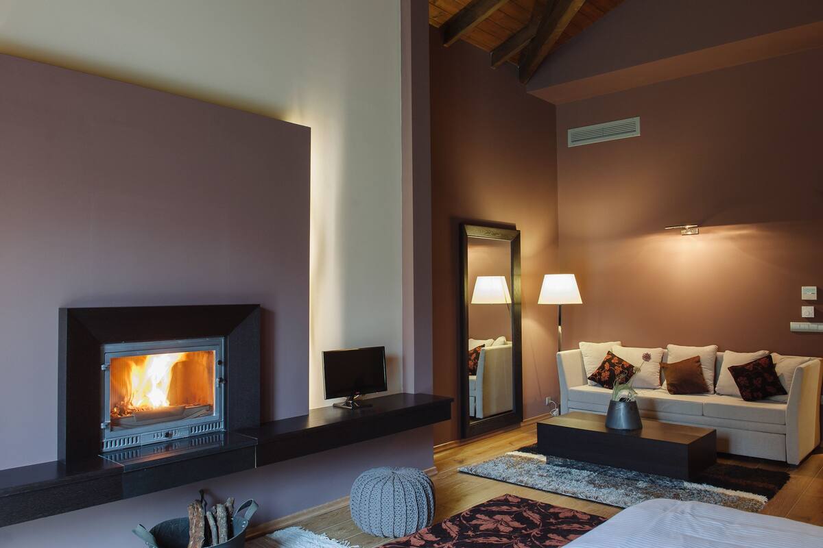 A cozy room with a fireplace, a sofa, a coffee table, and a mirror reflecting the room.