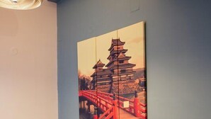A room with a purple sofa, a wall-mounted painting of a traditional Japanese bridge, and a hanging light fixture. - Porto Bello Design Hotel (Nafplio)
