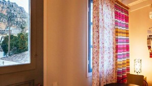 A room with a window, a table with two chairs, and a curtain with a floral pattern. - Porto Bello Design Hotel (Nafplio)