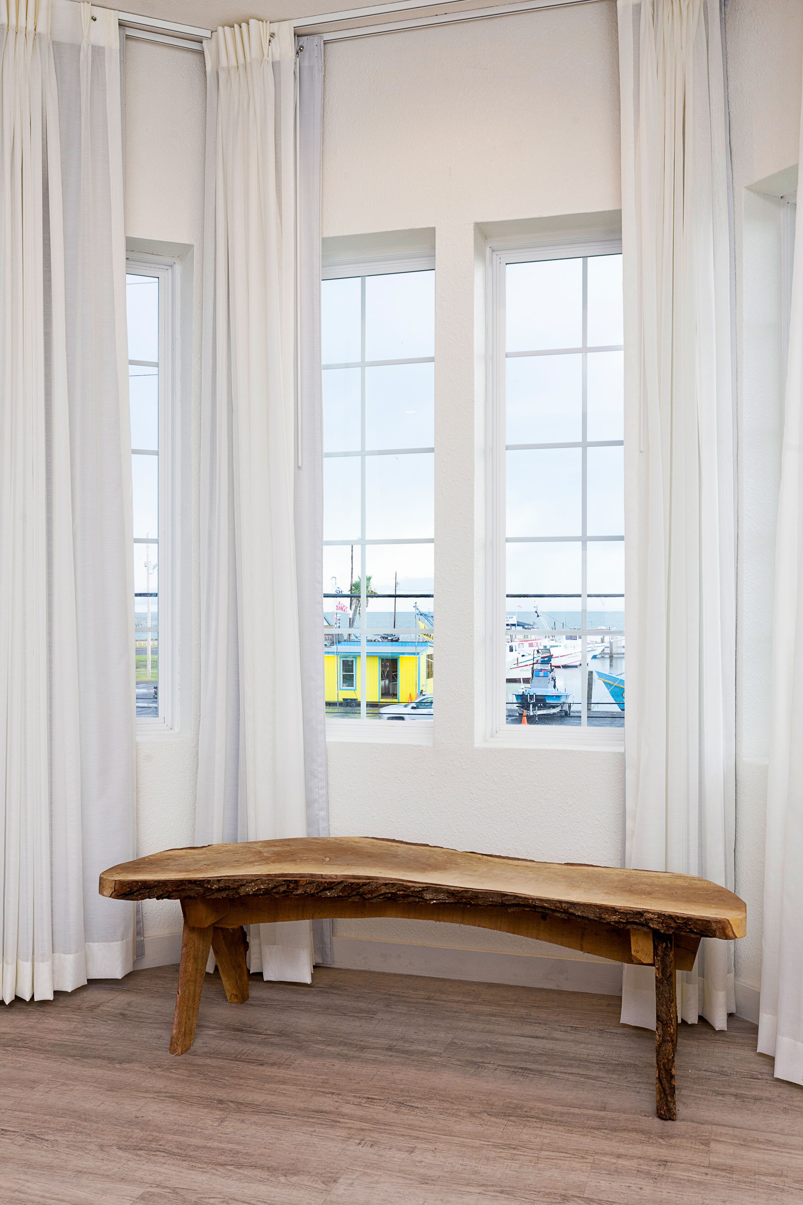 A room with a wooden bench, large windows, and white curtains.