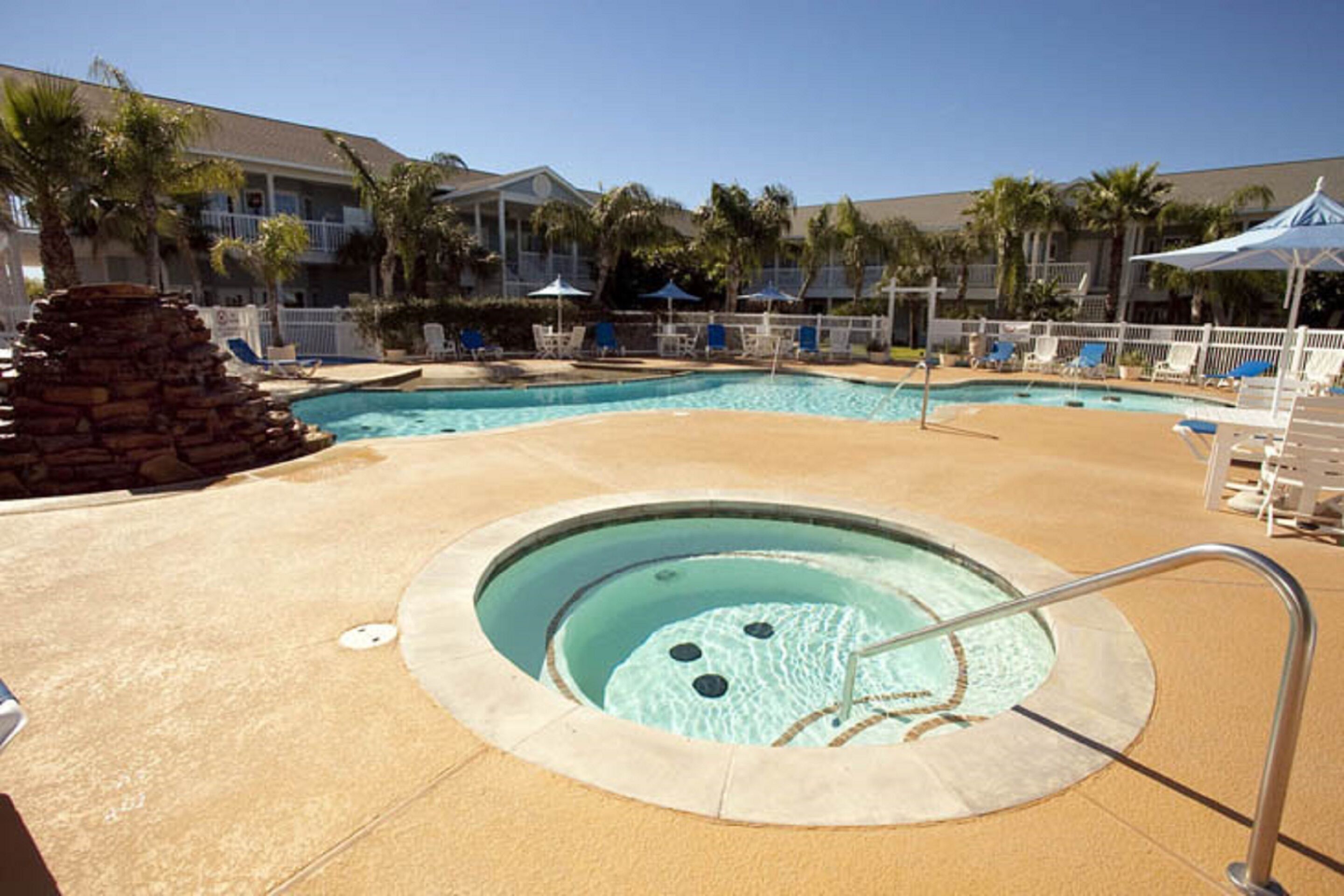 A pool area with a hot tub, lounge chairs, and umbrellas.