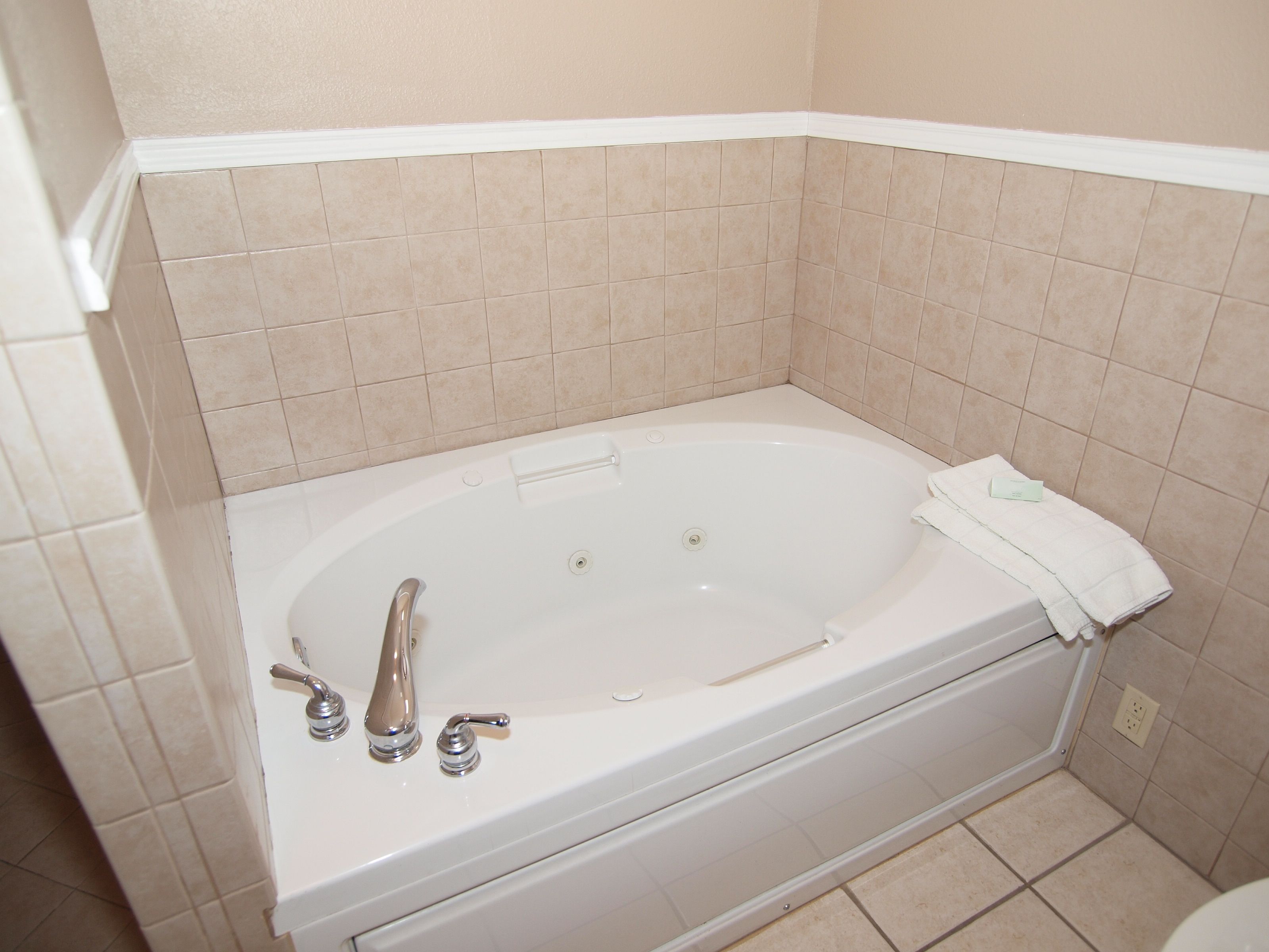 A bathroom with a white bathtub, two faucets, and a towel on the side.