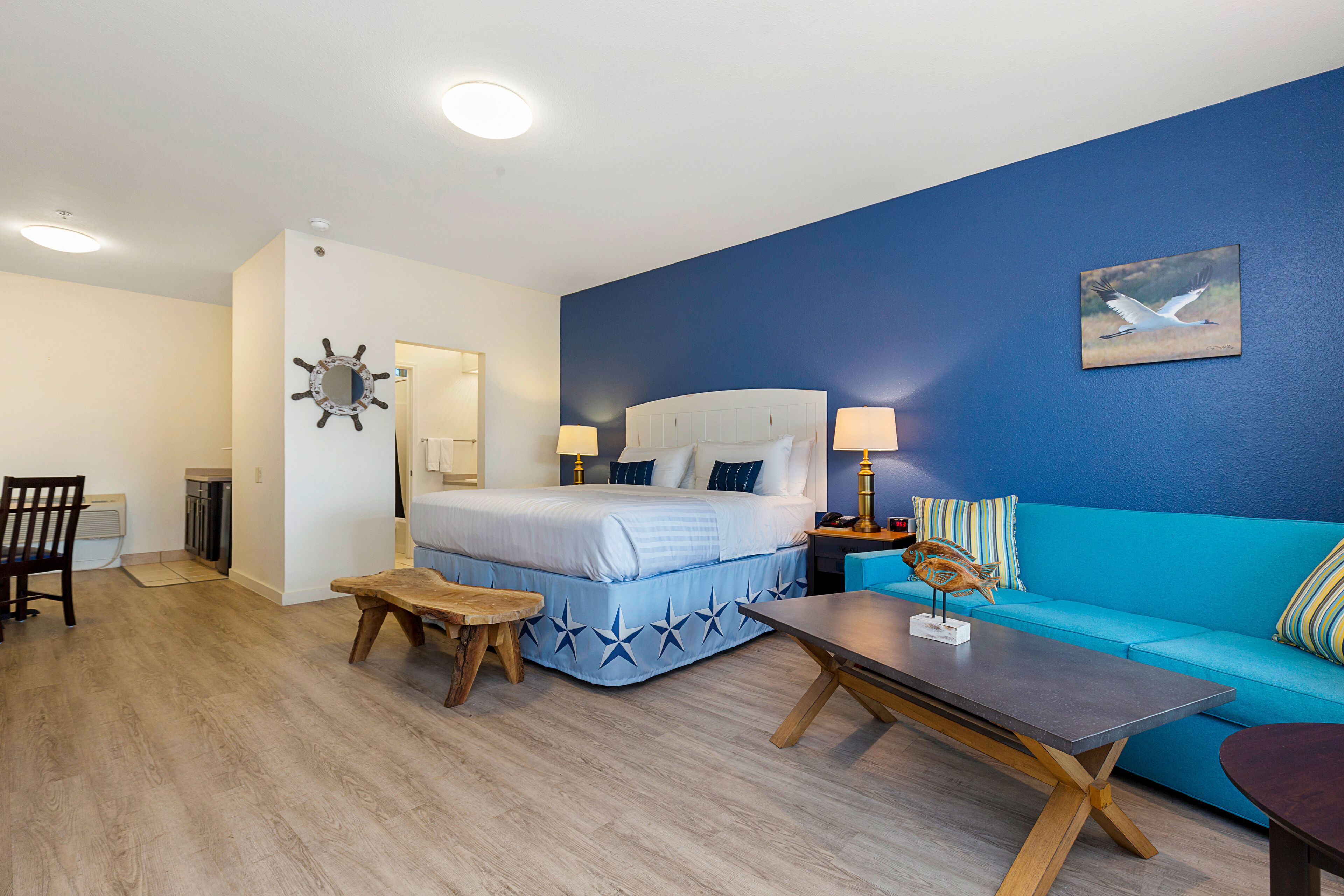 A bedroom with a bed, a blue sofa, a wooden table, and a nightstand with a lamp.