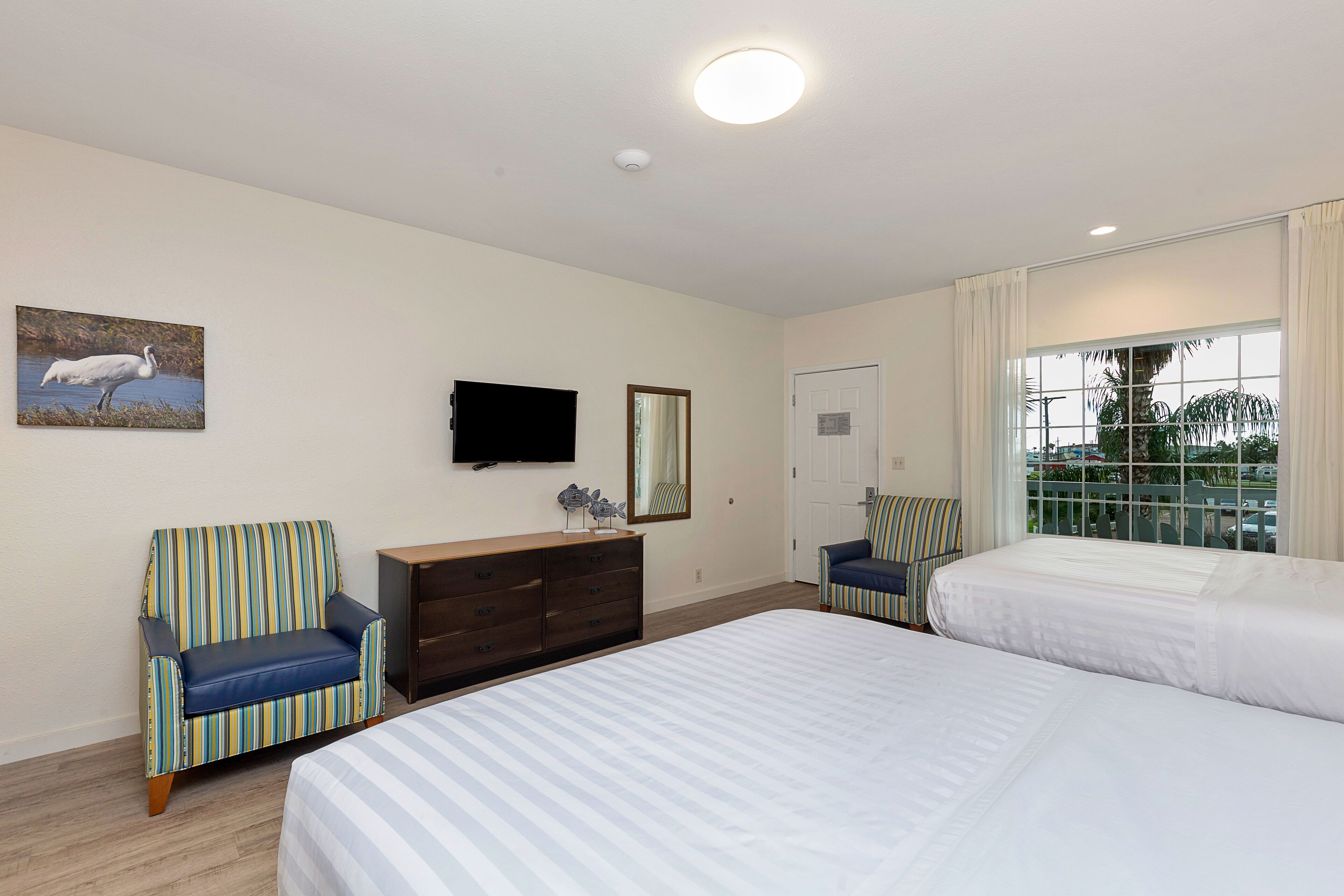 Une chambre d’hôtel avec deux lits, une télévision, une commode et une fenêtre donnant sur des palmiers.