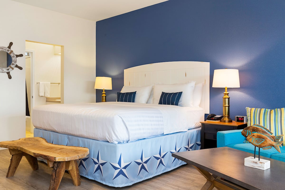 A hotel room with a large bed, two bedside lamps, a wooden bench, a small table with a decorative fish, and a blue-striped sofa.