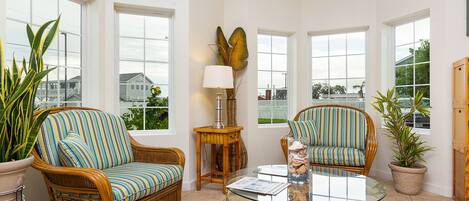 Una habitación luminosa con muebles de mimbre, ventanas amplias y plantas en macetas.