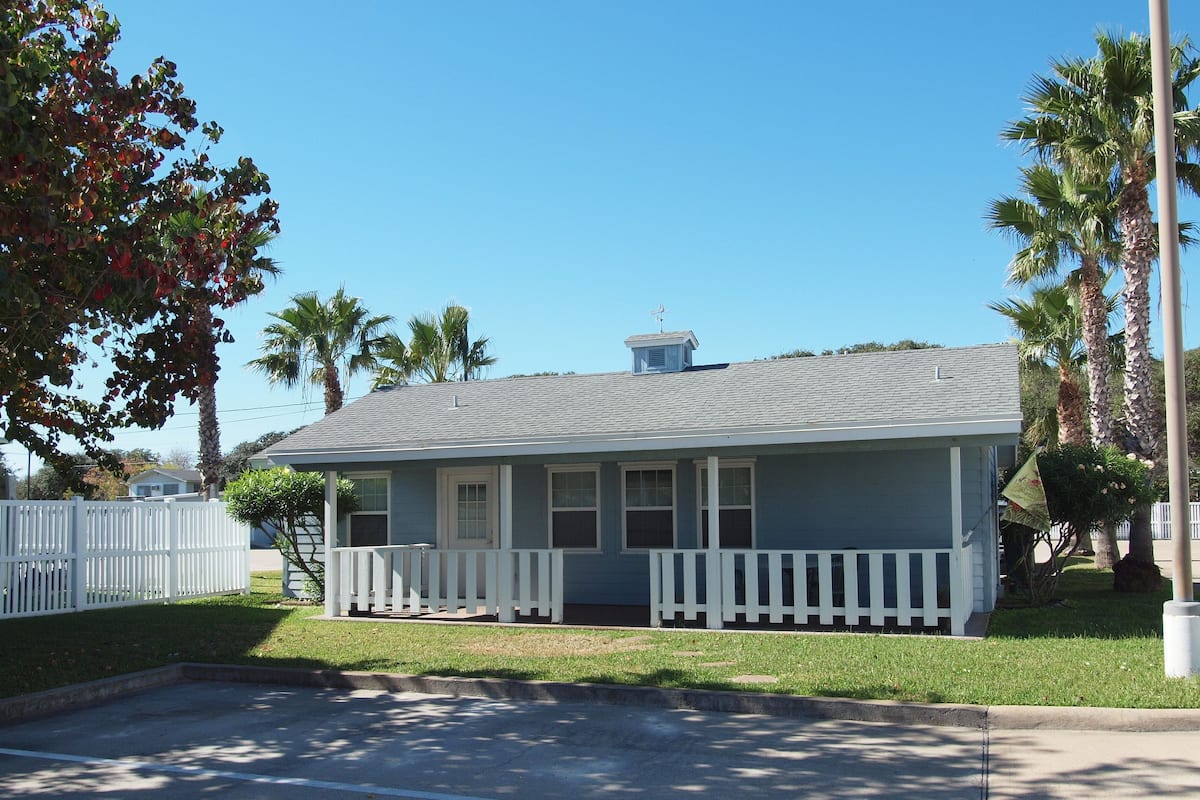 A single-story house with a gabled roof, a front porch with white railings, and a small attached garage.