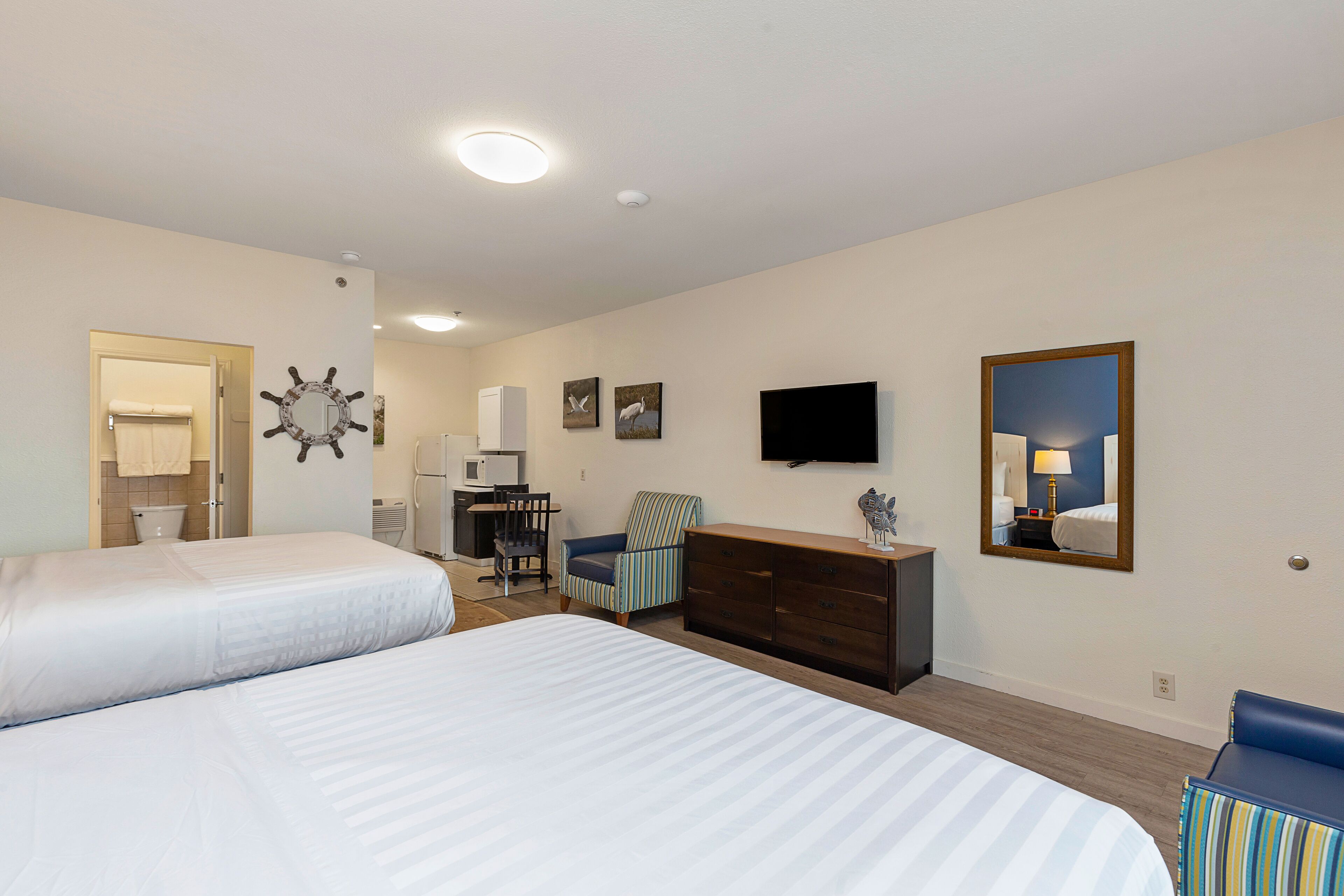 Une chambre d’hôtel avec deux lits, un bureau, une commode, une chaise, une télévision et un miroir.
