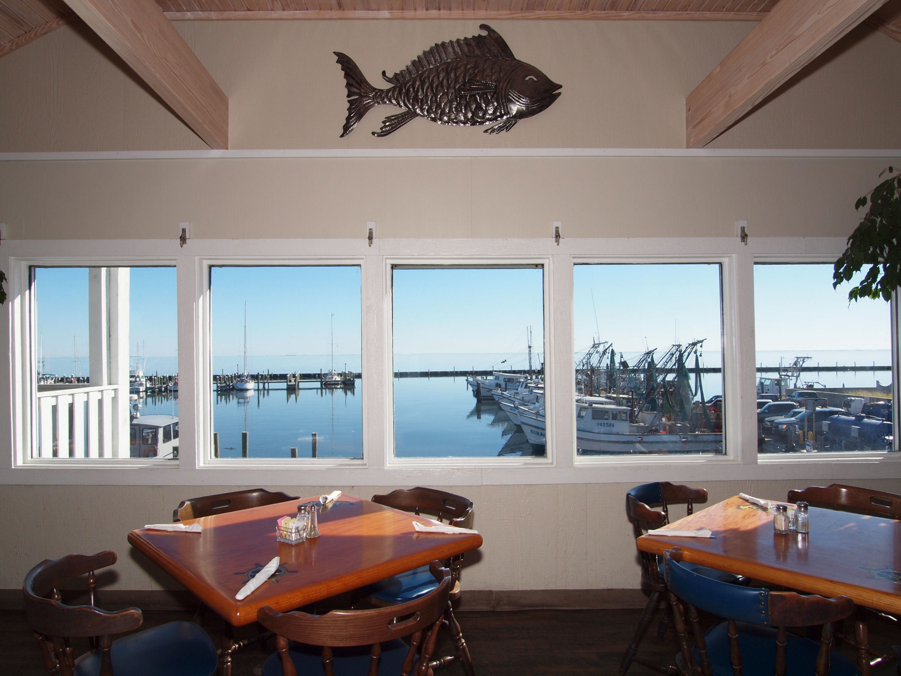 A dining area with a view of a marina through large windows, wooden tables, and chairs.
